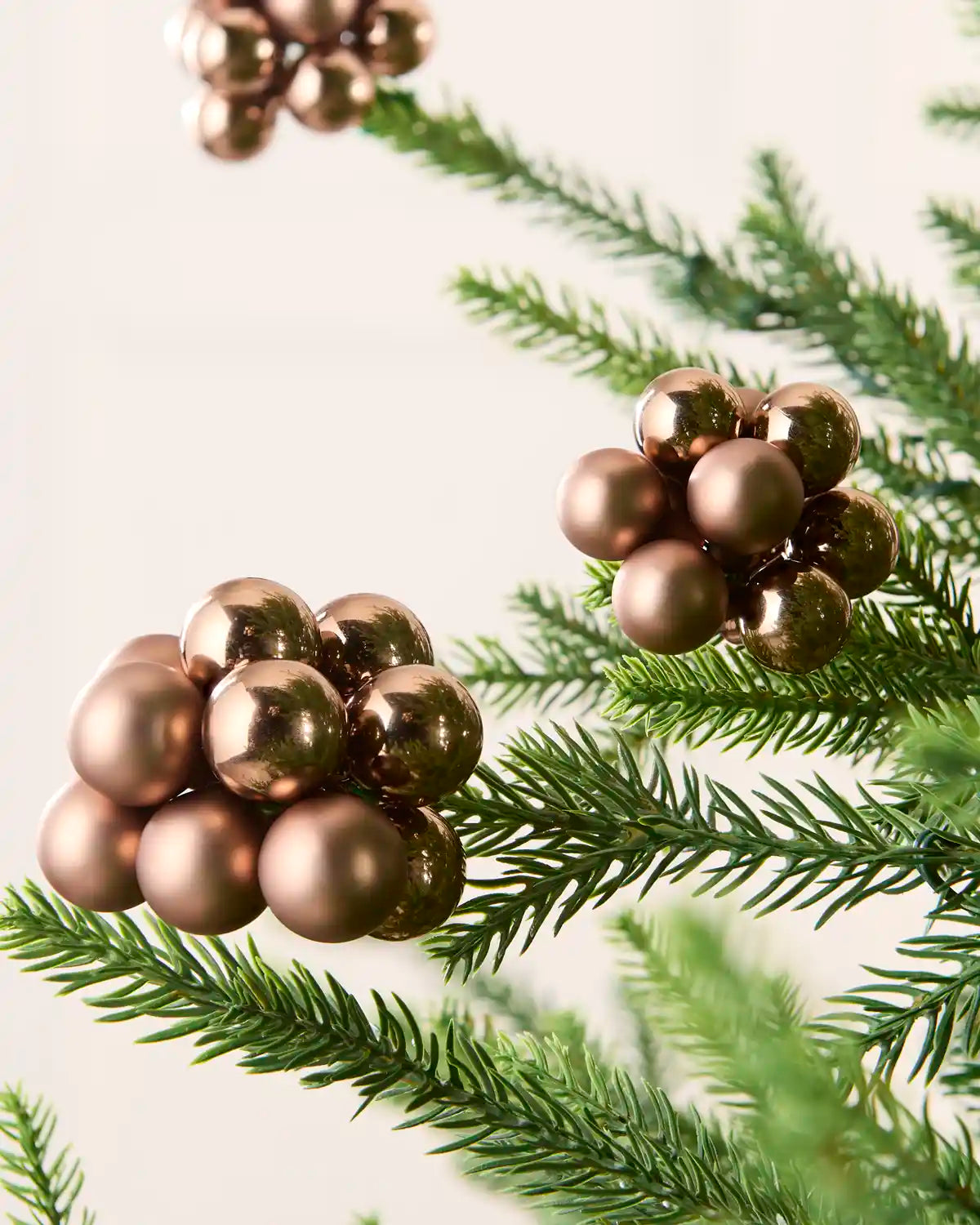 Mocha cluster baubles on a Christmas tree branch with other cluster baubles in background against a cream wall