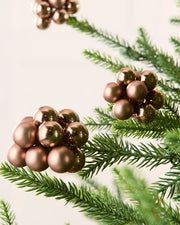 Mocha cluster baubles on a Christmas tree branch with other cluster baubles in background against a cream wall