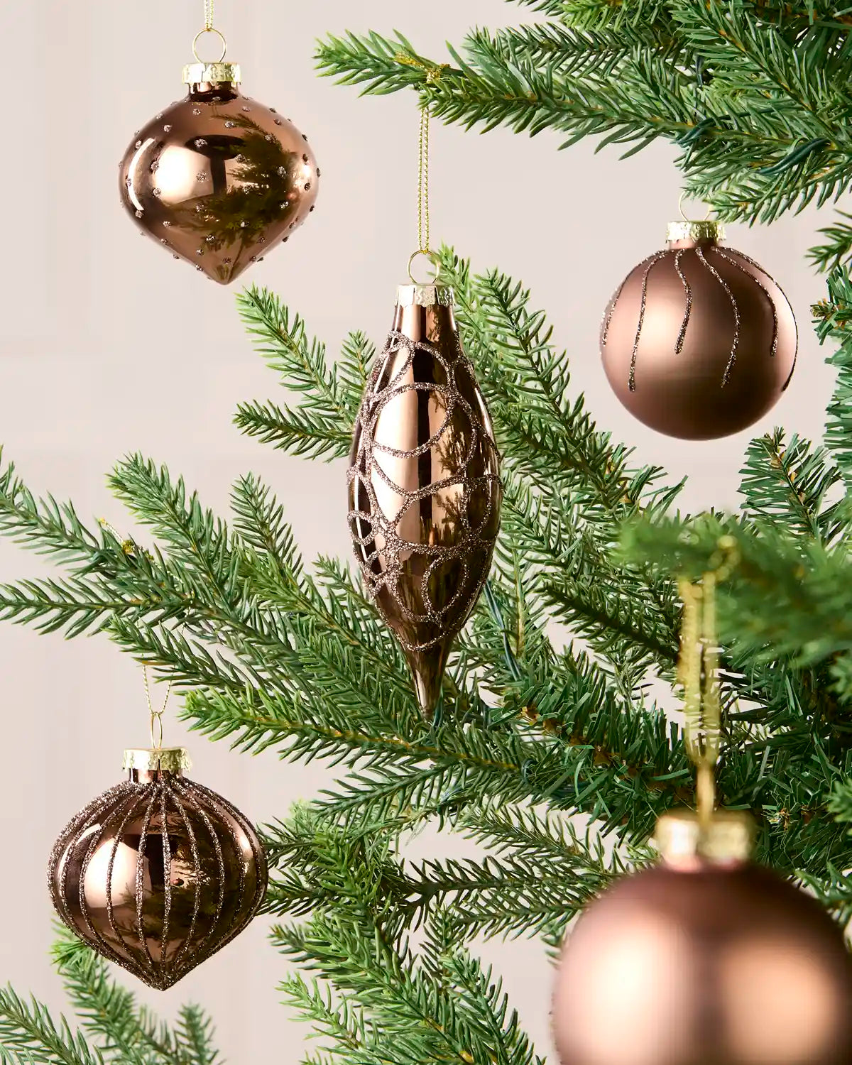 Mocha coloured Glass baubles hanging with gold string on a Christmas tree against a cream background