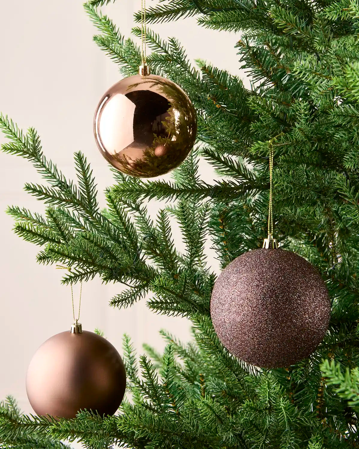 Mocha coloured baubles hanging on a Christmas tree branch against a cream background