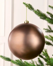 Mocha coloured oversized bauble hanging on a Christmas tree branch against a cream background