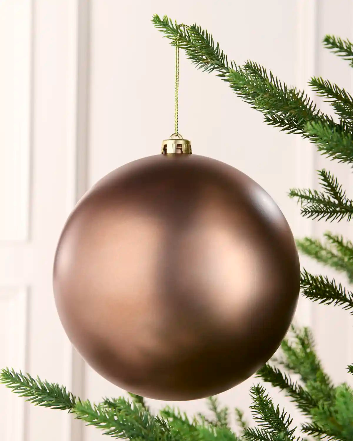 Mocha coloured oversized bauble hanging on a Christmas tree branch against a cream background