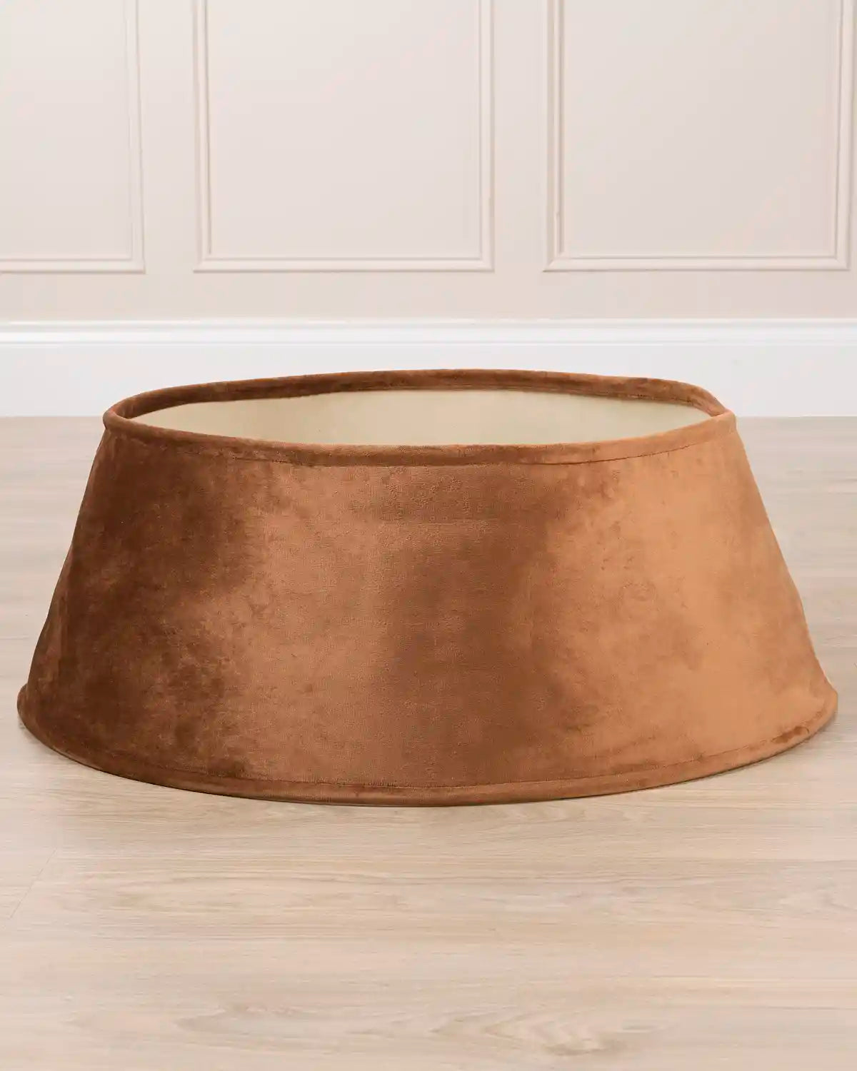 Mocha coloured velvet tree skirt with a wide, flared dome shape, shown on a light wood floor against a white panelled wall.