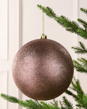 Mocha oversized glitter bauble hanging on a Christmas tree against a cream wall