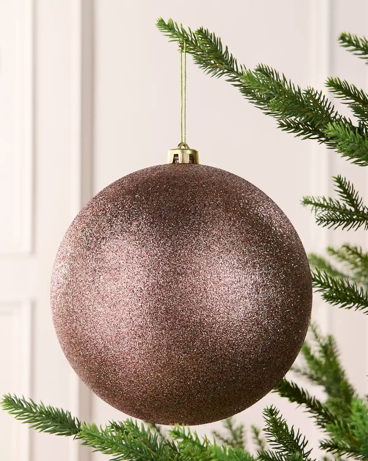 Mocha oversized glitter bauble hanging on a Christmas tree against a cream wall