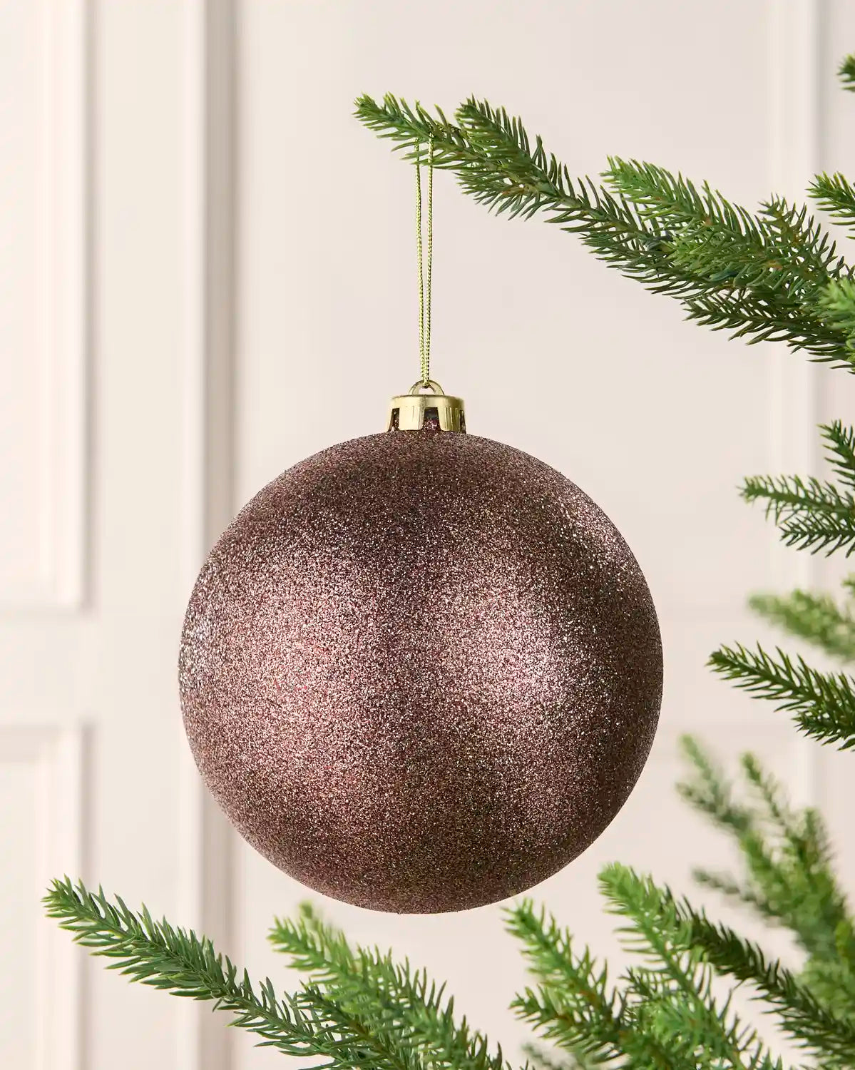 Mocha oversized glitter bauble on a Christmas tree branch against a cream wall
