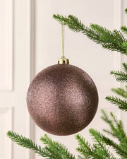 Mocha oversized glitter bauble on a Christmas tree branch against a cream wall