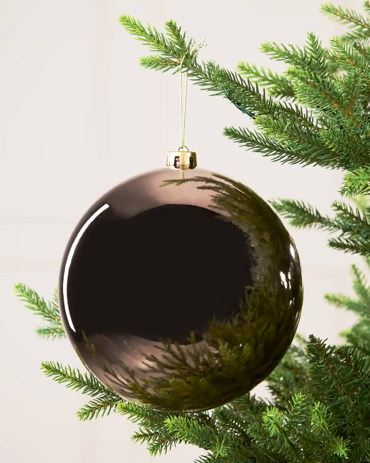 Mocha shiny oversized bauble hanging on a Christmas tree branch against a ream background