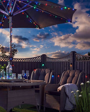 Multi colour string lights on an outdoor umbrella in a garden with blue sky and clouds 