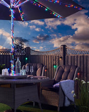Multi coloured LED fairy lights on an umbrella with garden furniture and cloudy blue sky