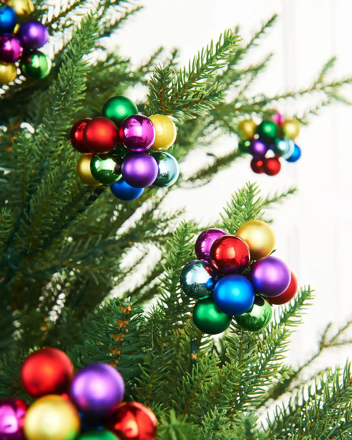 Multi coloured berry cluster baubles on a Christmas tree with a white background