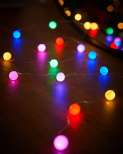 Multi coloured berry string lights on a wooden table with a mirror in background