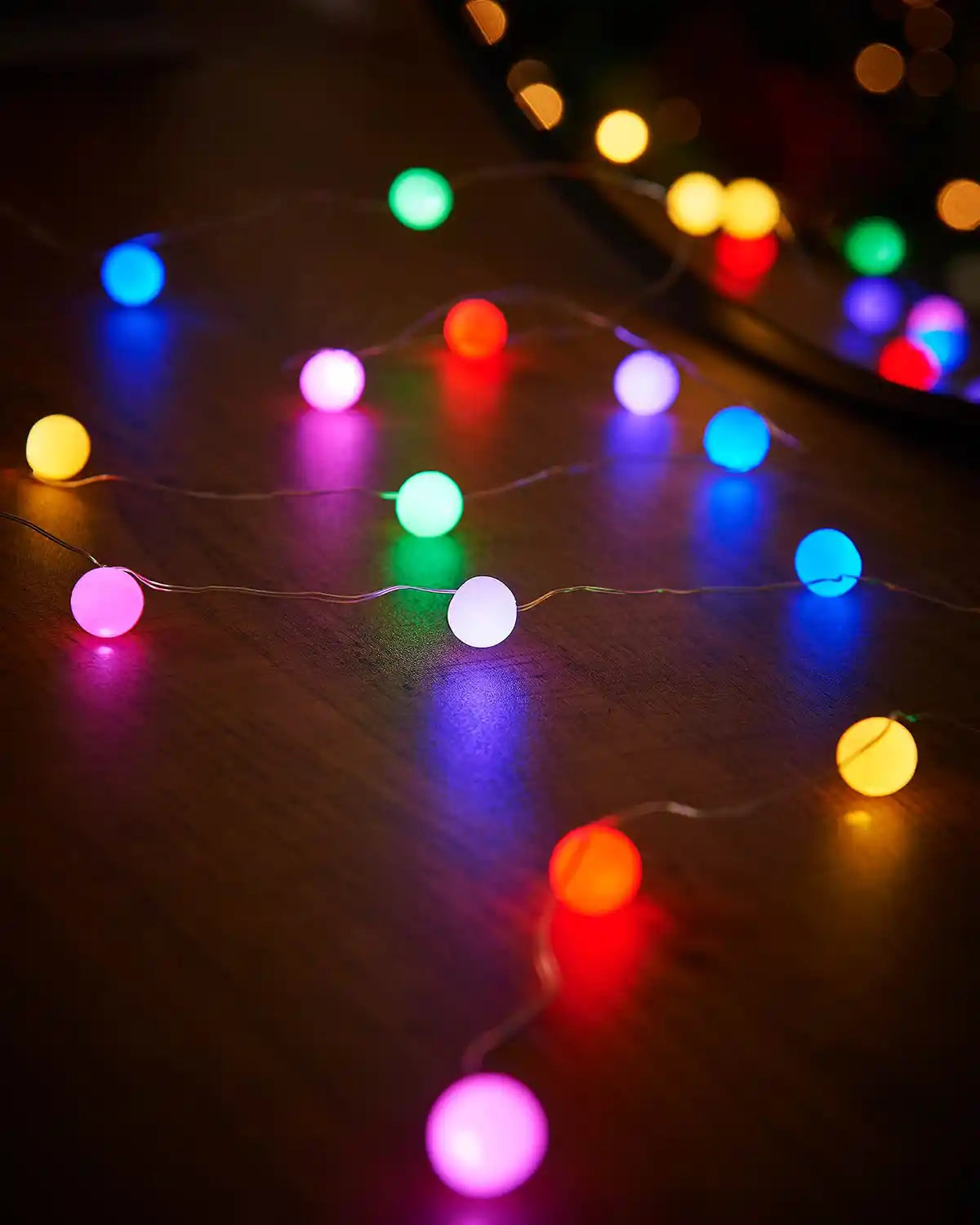 Multi coloured berry string lights on a wooden table with a mirror in background