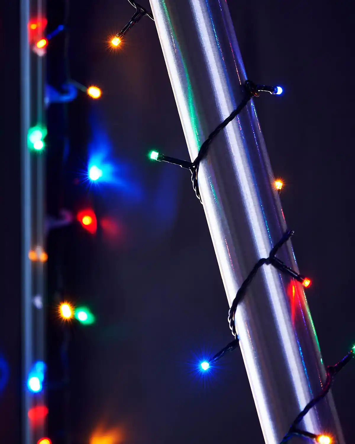 Multi coloured string lights wrapped around a metallic pole against a dark background