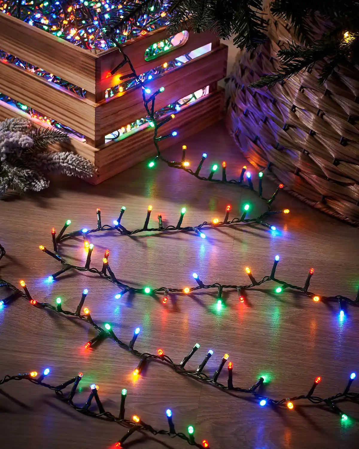 Multicoloured string lights on a wooden surface with a wicker basket and Christmas tree decorations.