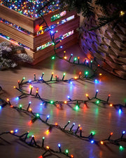 Multicoloured string lights on a wooden surface with a wicker basket and Christmas tree decorations.