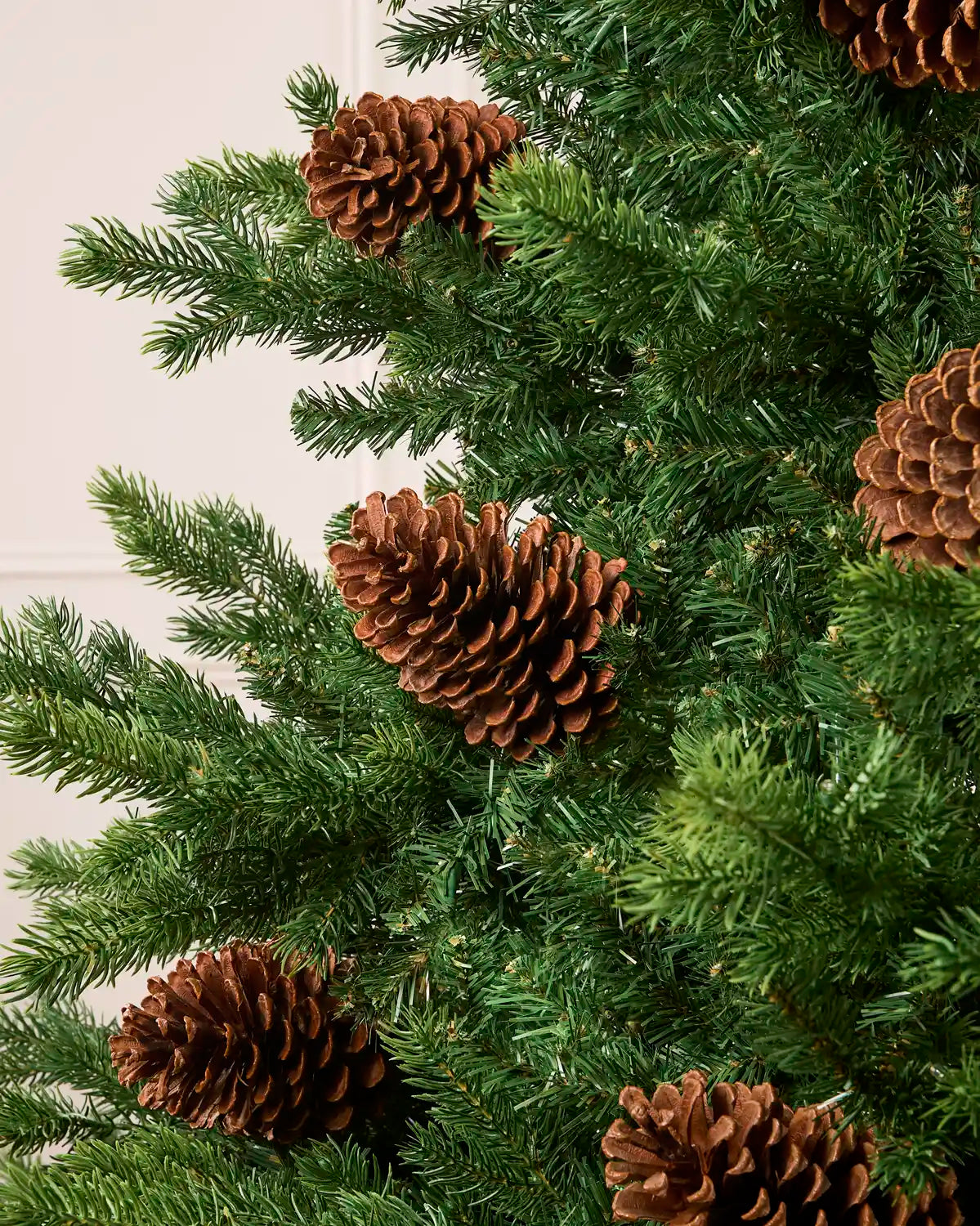 Multiple large pinecones placed on Christmas tree branches with a blurred cream background