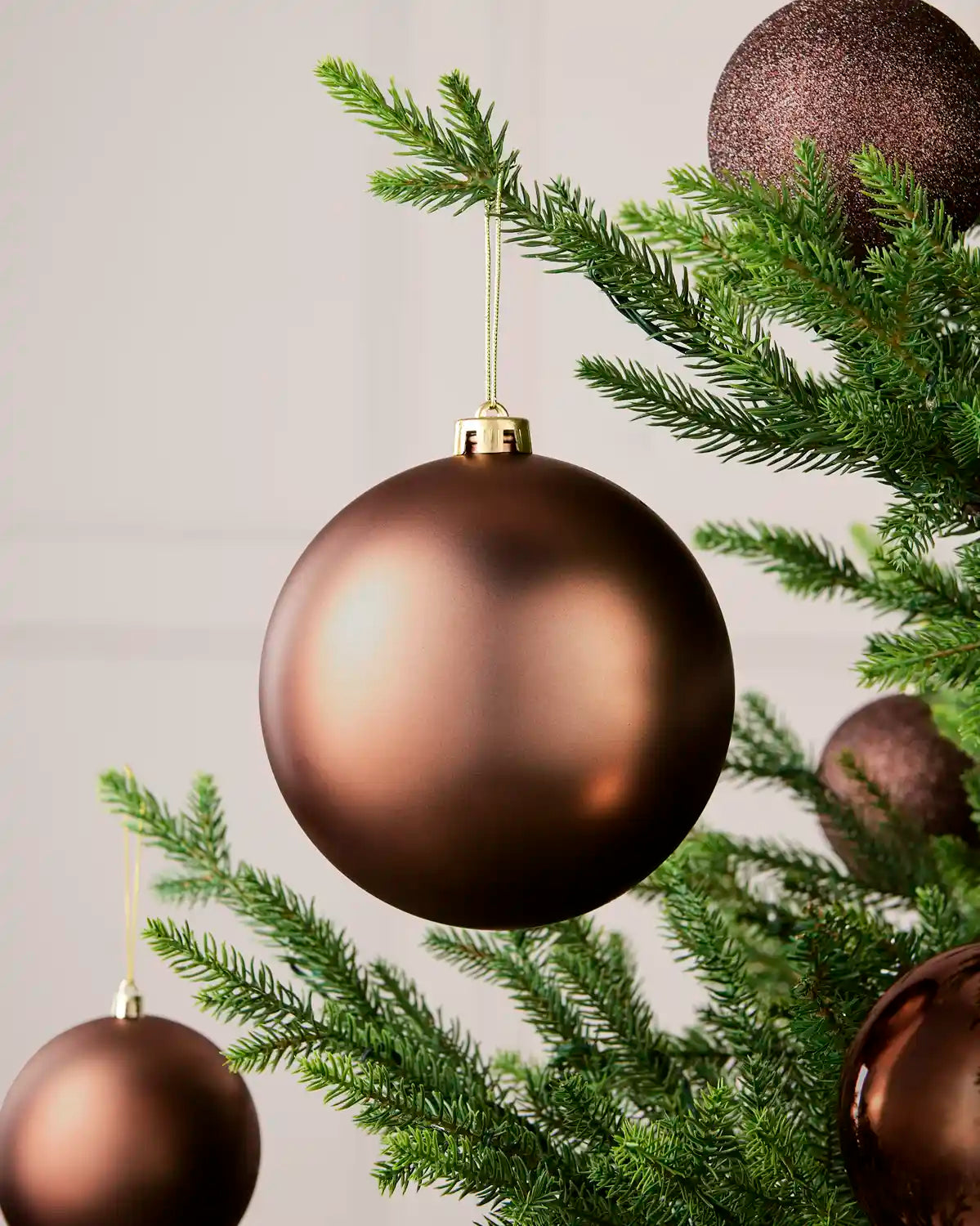 Multiple oversized espresso baubles hanging on a Christmas tree against a cream background