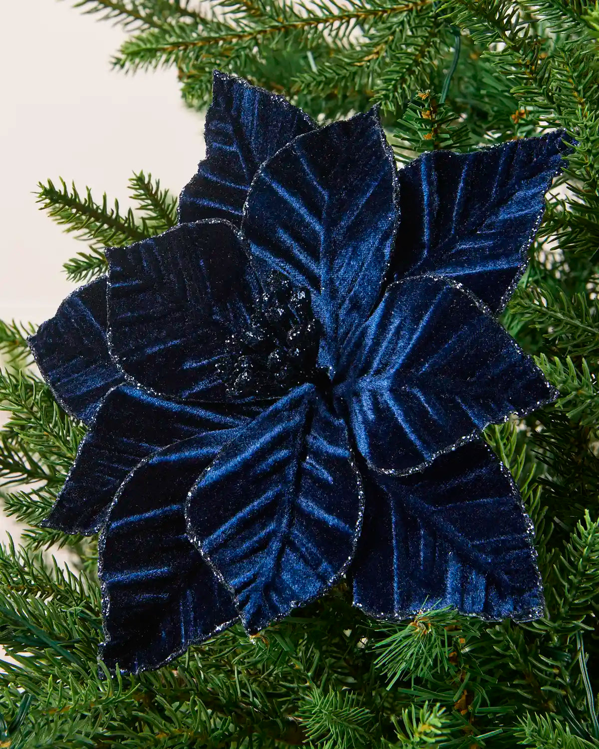 Navy Blue Poinsettia with a glitter border on a Green Christmas tree against and cream panel background
