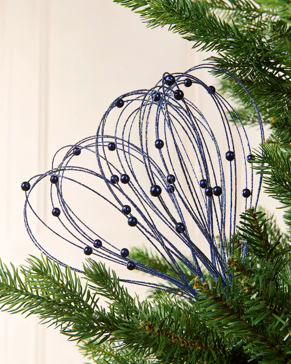Navy Glitter Nest Christmas Tree Pick placed in green Christmas tree branches with a cream background
