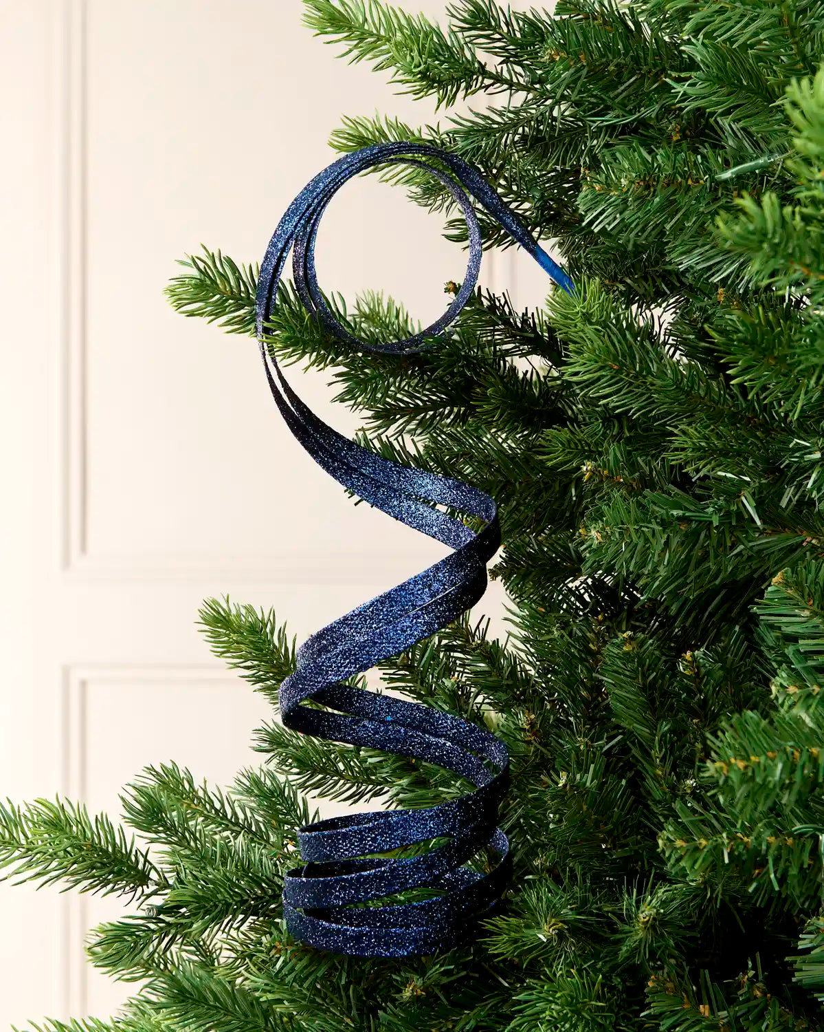 Navy Glitter Spiral Swirl Pick hanging from Christmas tree branch with cream background

