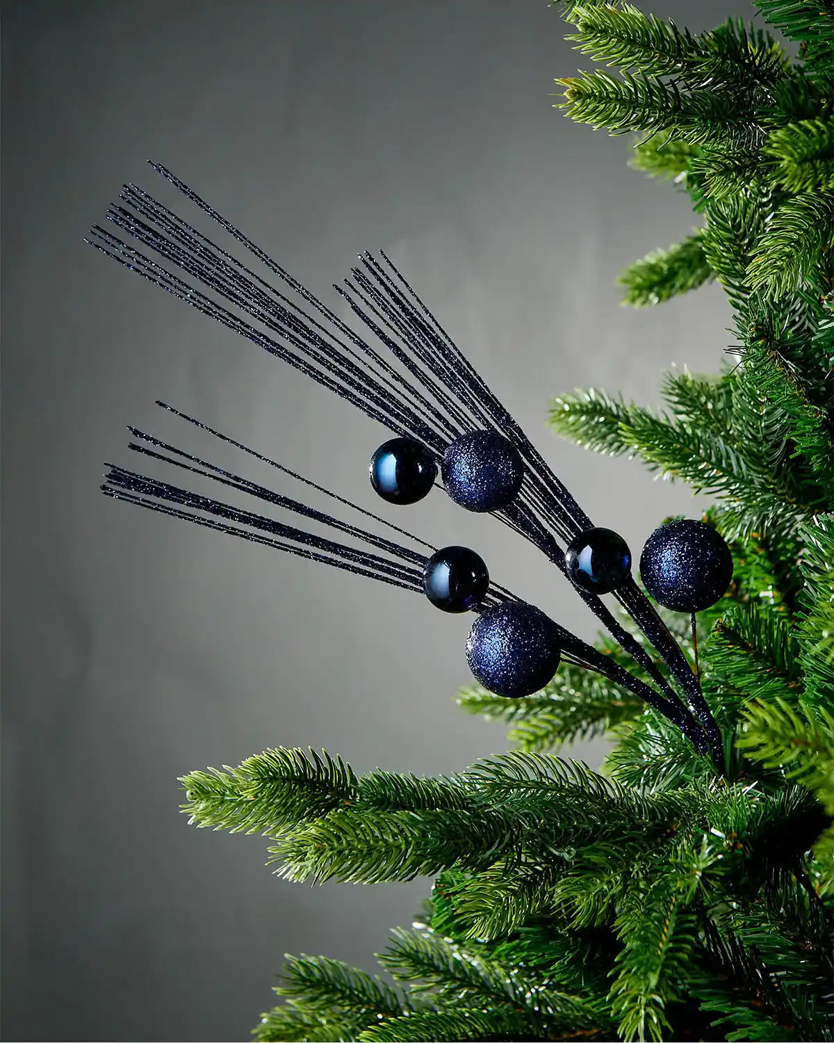 Navy blue glitter bauble spray inside Christmas tree with grey background