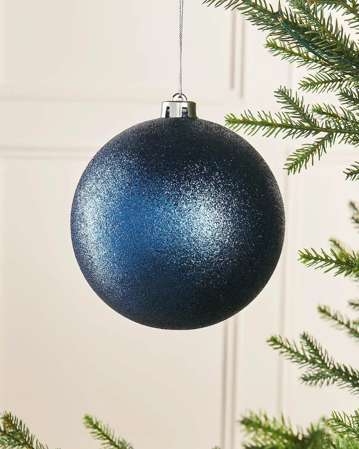 Navy blue glitter oversized 15cm bauble on a Christmas tree branch