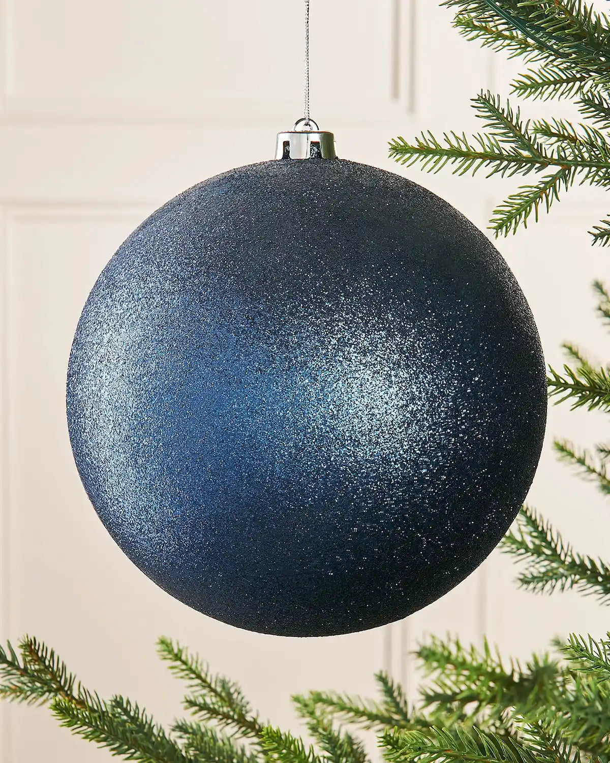 Navy blue glitter oversized bauble on a Christmas tree branch