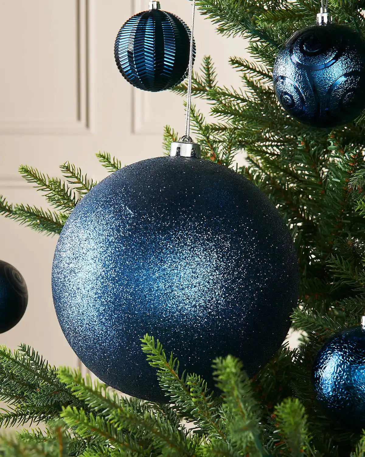Navy blue glitter oversized bauble on a Christmas tree branch with 4 smaller navy blue baubles in background