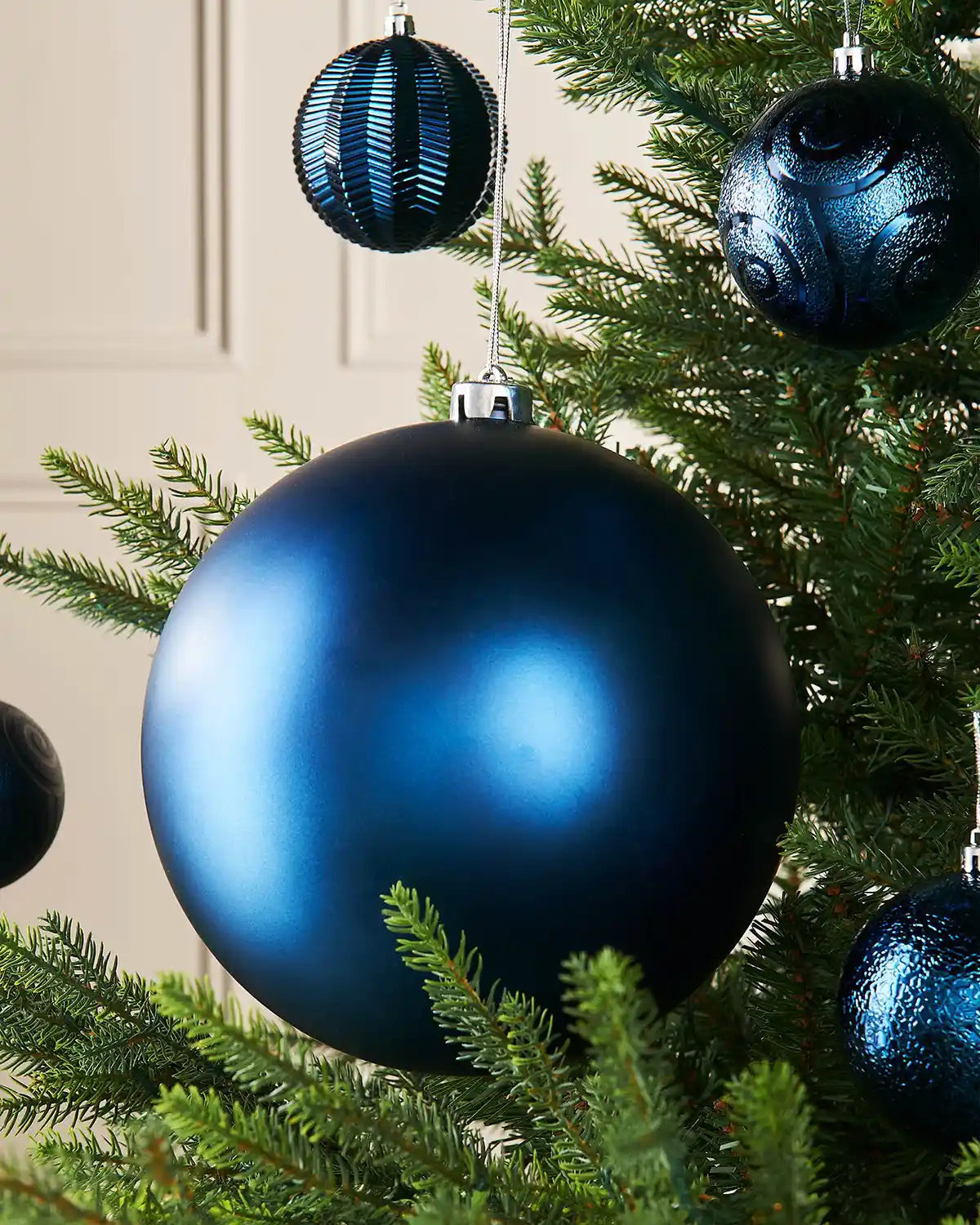 Navy blue oversized bauble on a Christmas tree branch with 4 smaller blue baubles in the background