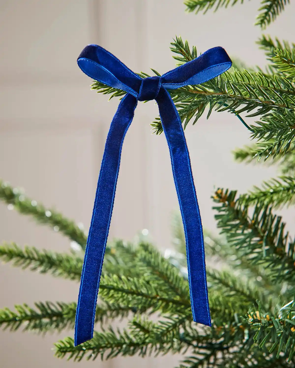 A single navy blue velvet bow on the edge of a Christmas tree branch, in front of a white background