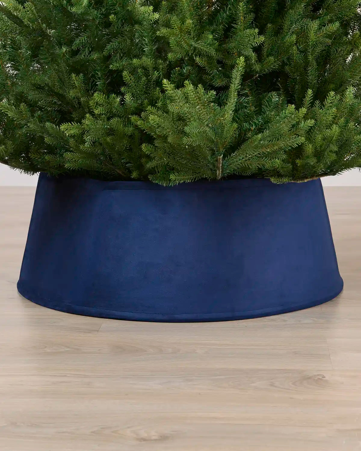 Navy coloured velvet tree skirt under a Christmas tree on a Light brown floor
