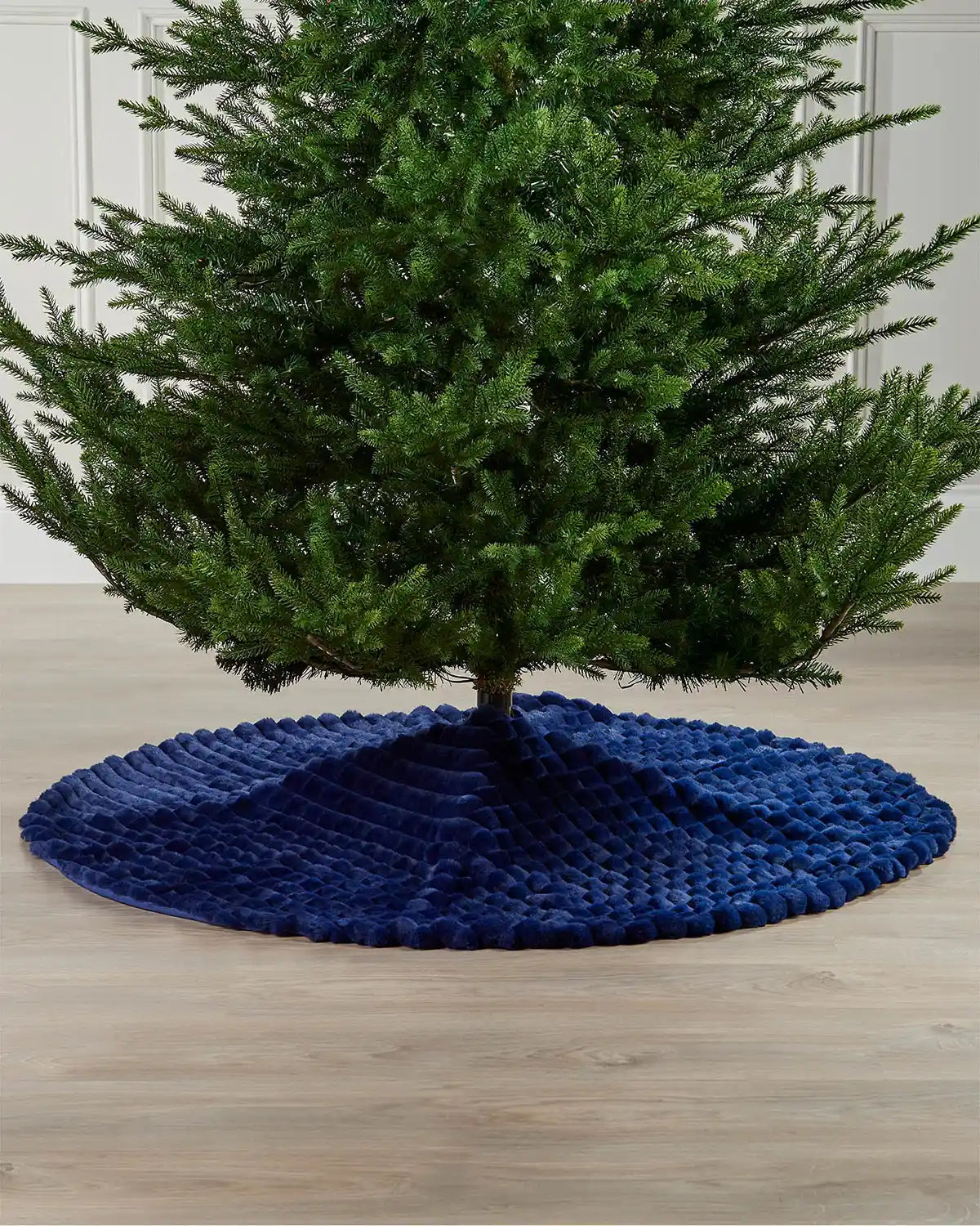 Full view of the navy faux fur diamond tree skirt on light wooden flooring underneath a green Christmas tree