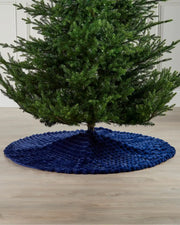 Full view of the navy faux fur diamond tree skirt on light wooden flooring underneath a green Christmas tree