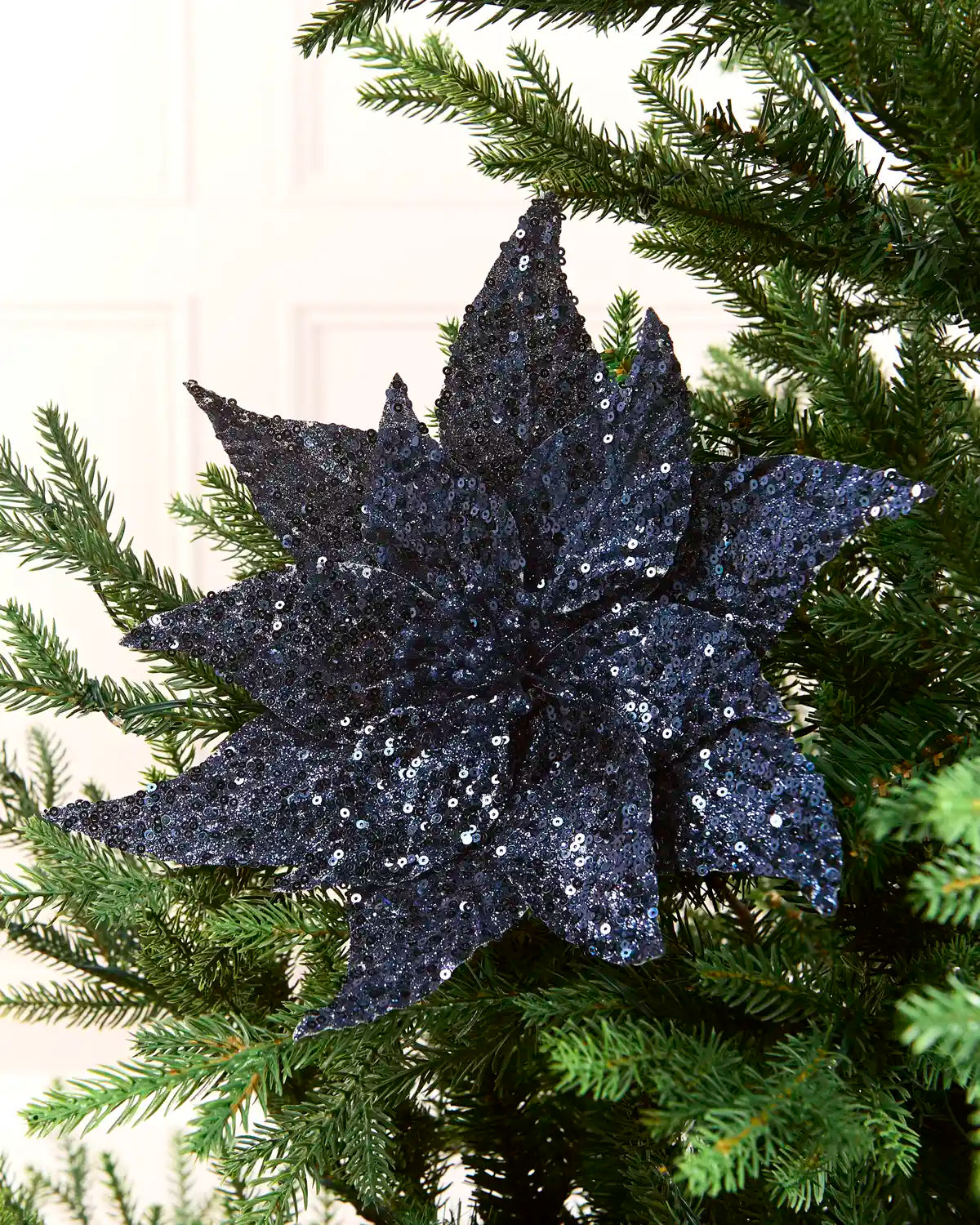 Navy sequin poinsettia on a Christmas Tree against a light background