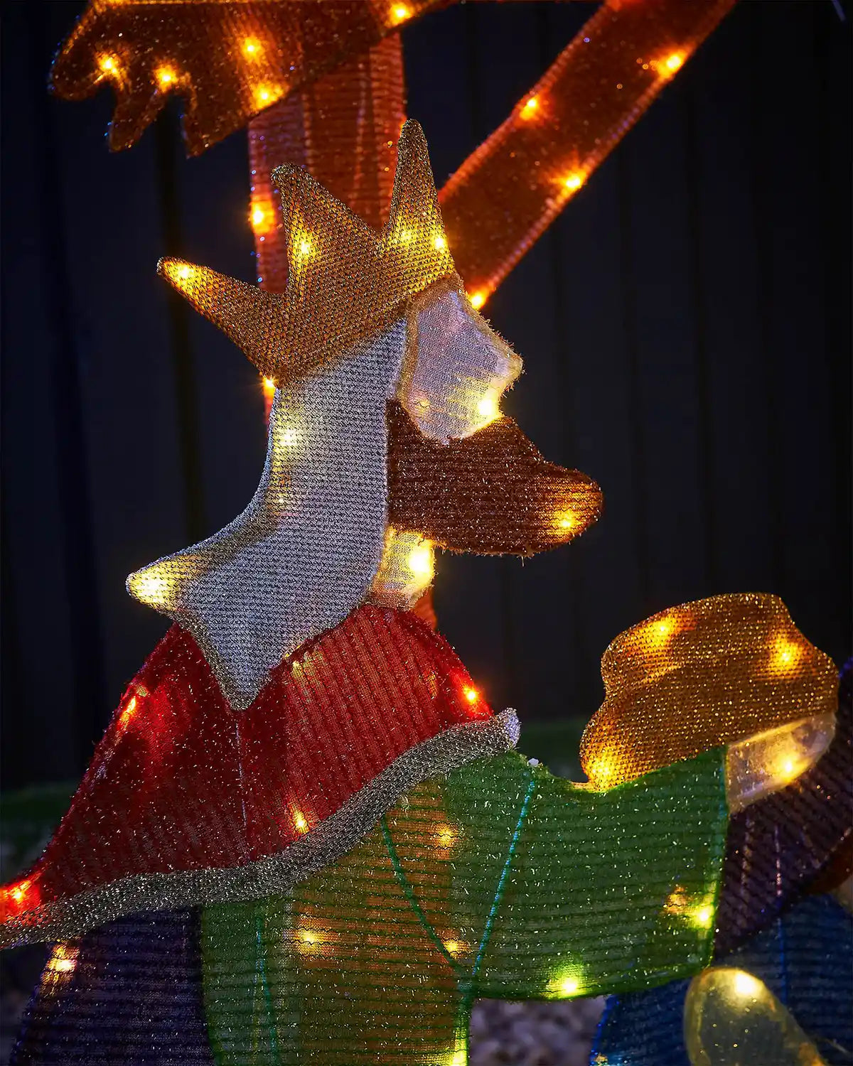 One of the three kings holding gold bar covered in LED lights against a dark background