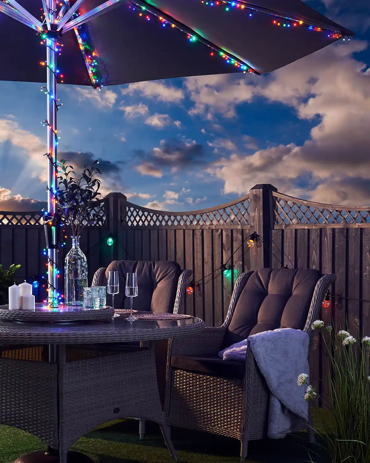 Outdoor patio set with multi colour LED fairy lights umbrella and table under a cloudy sky