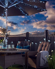 Outdoor patio setting with a large umbrella wrapped in ice white string lights, table, and chairs under a cloudy sky.