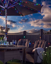 Outdoor patio setting with a lit with multi coloured strong lights on umbrella pole with and table under a cloudy sky