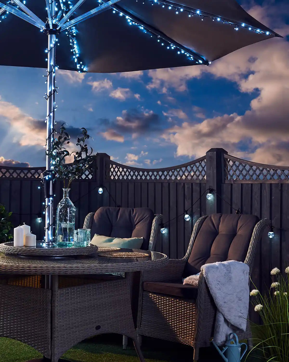 Outdoor patio setting with ice white string lights, table, chairs, and a cloudy sky.