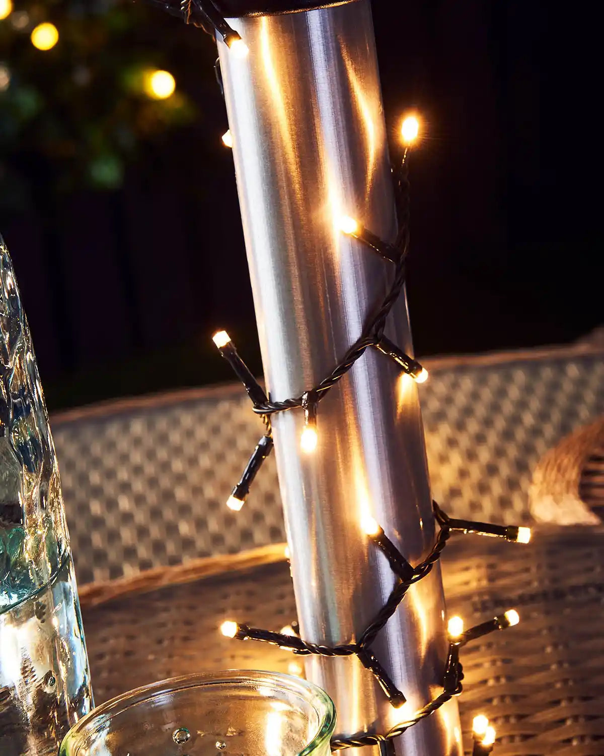 Outdoor umbrella with warm white string lights draped over it against a dark background