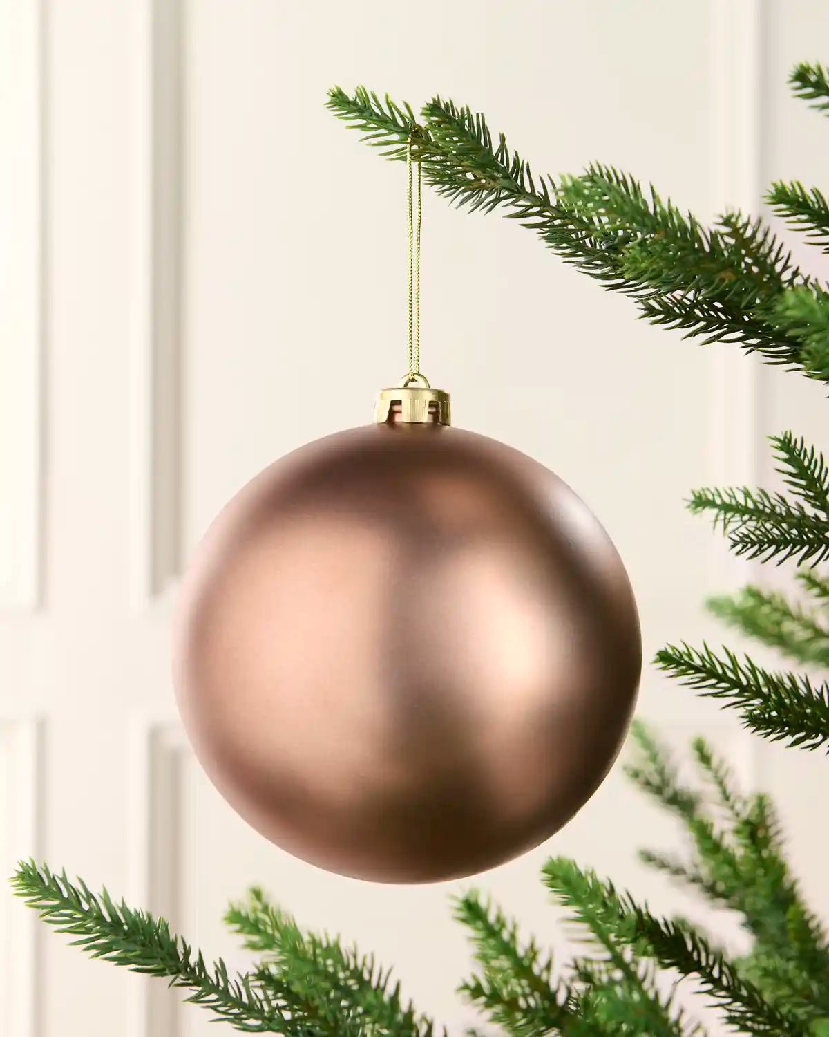 Oversized Bauble hanging from a Christmas tree against a cream background