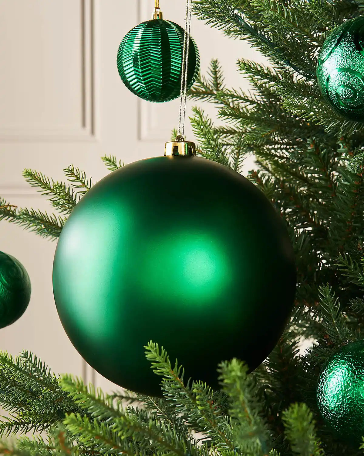 Oversized Christmas green matt bauble on a Christmas tree branch with 4 smaller green baubles in the background
