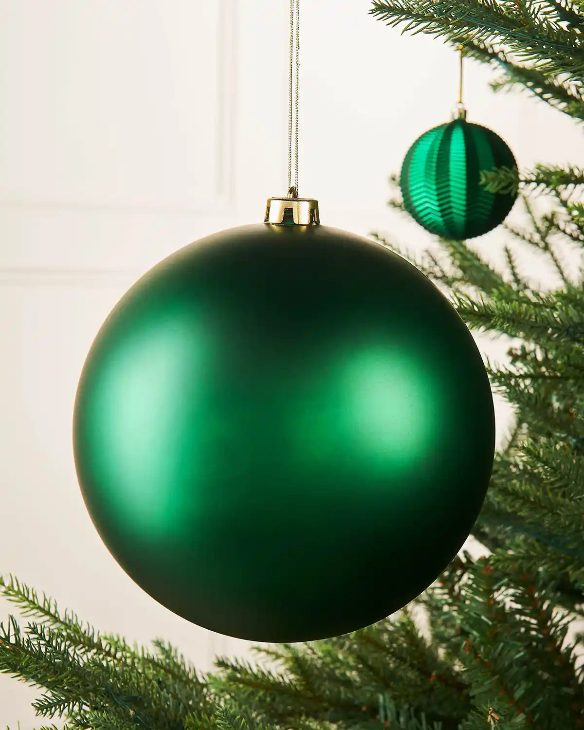 Oversized Christmas green matt bauble on a Christmas tree branch with a smaller green bauble in the background