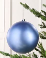 Oversized Ice blue bauble on a Christmas tree branch against a cream background