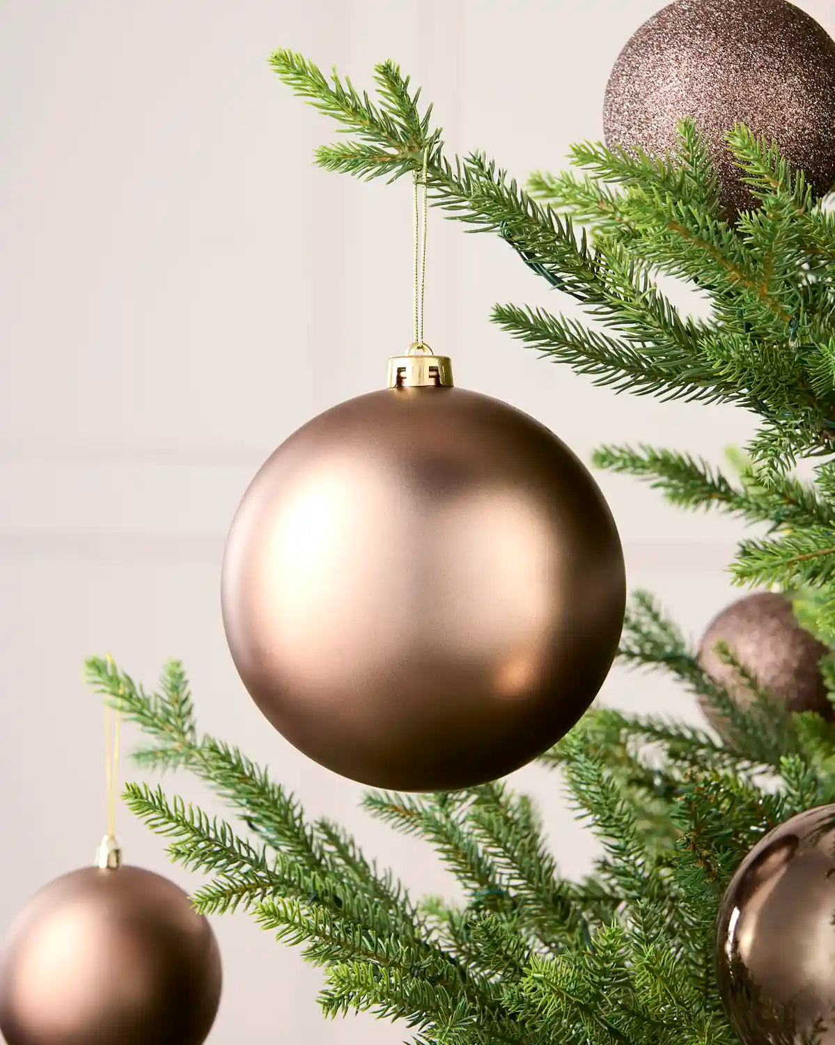 Oversized Mocha bauble matt effect on a Christmas tree with smaller baubles in the background against a cream background