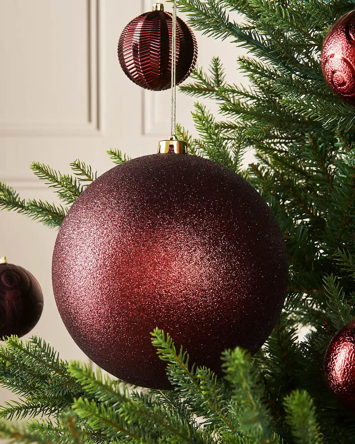 Oversized glitter Burgundy bauble on a Christmas tree branch with 4 smaller burgundy baubles in background