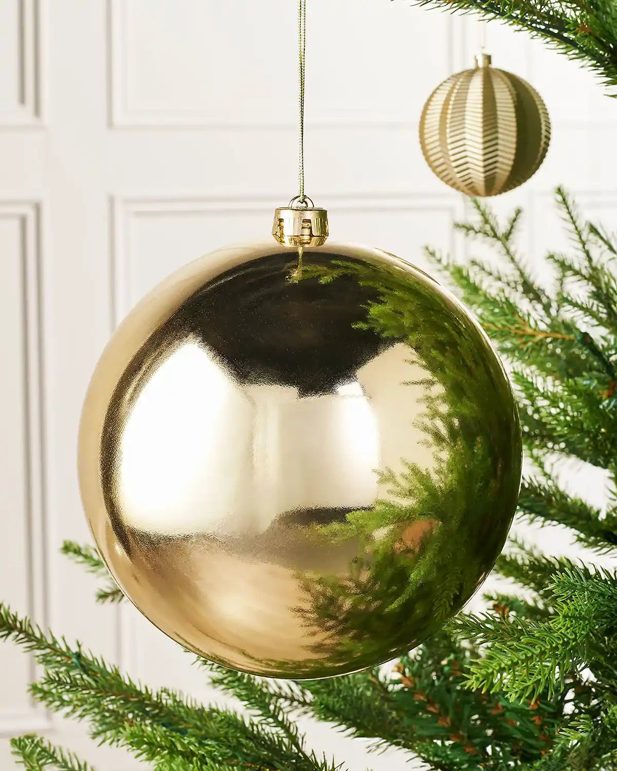 Oversized gloss gold bauble on a Christmas tree branch and a smaller gold bauble 