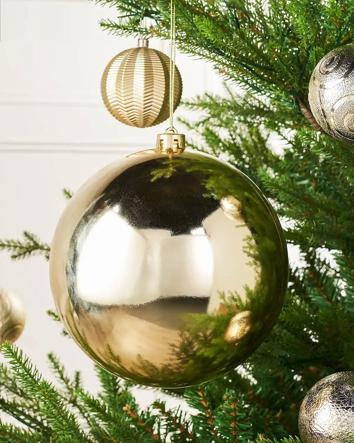 Oversized gloss gold bauble on a Christmas tree branch and a smaller gold bauble with 4 smaller baubles