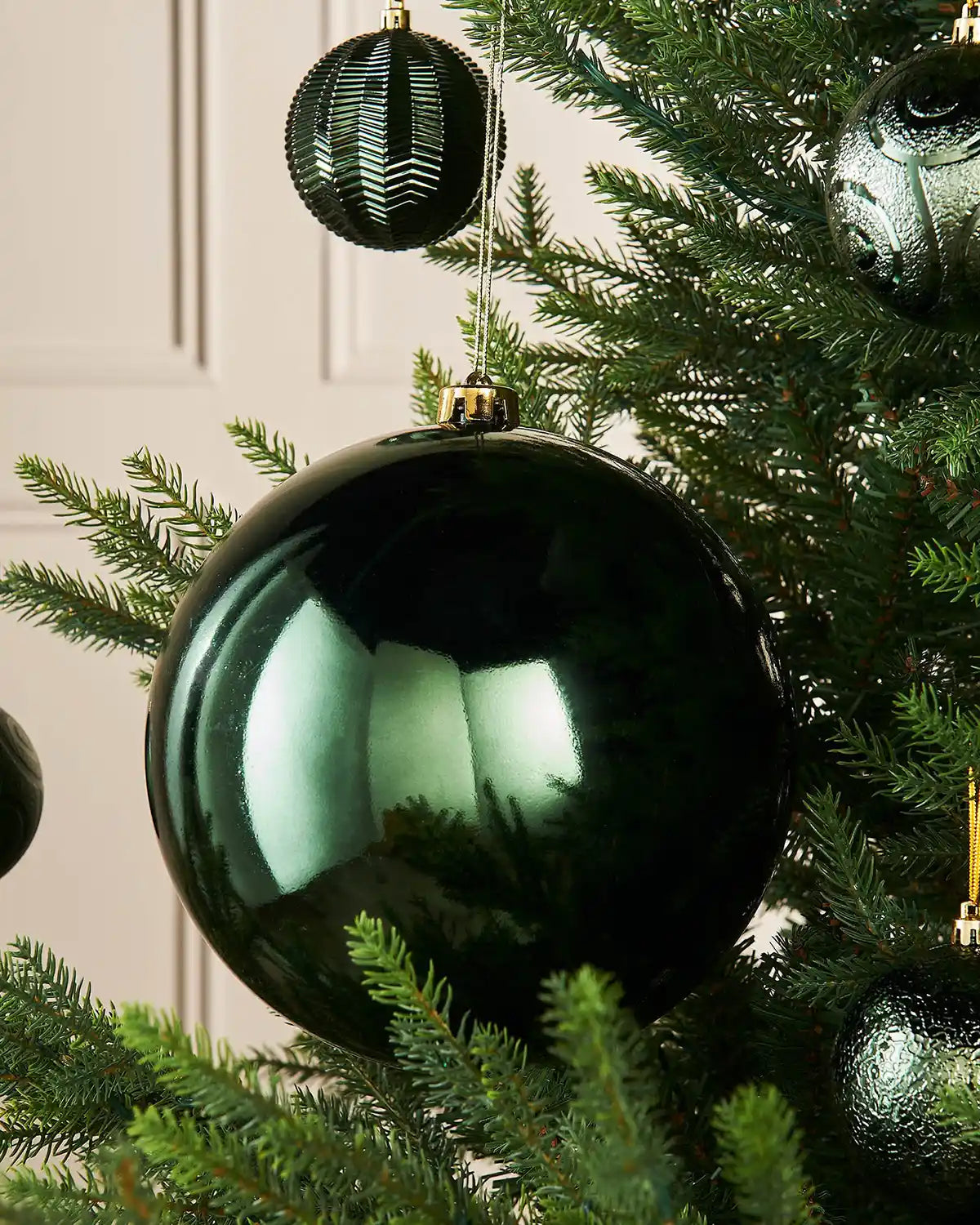 Oversized gloss green bauble on a Christmas tree branch with 4 smaller green baubles in background